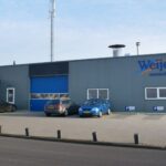 Bedrijfspand van Autoschade Weijer met blauwe deur en geparkeerde auto's voor het gebouw.